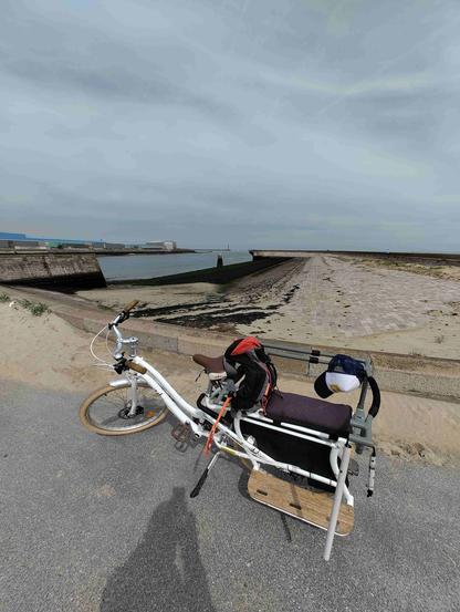 Au premier plan un vélo cargo, en fond une jetée et chenal donnant sur la mer.