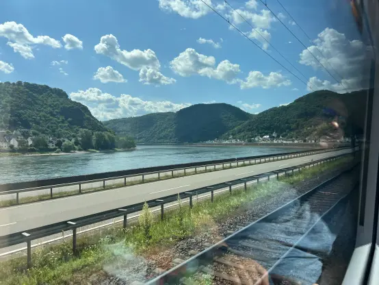 view out a train window, down a curve of the Rhine. the rail line passes right next to the shore, just separated by a single road