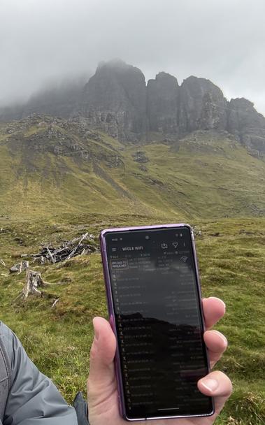 The peak of the Old Man of Stoor is in the background, a phone running the WigleWiFi app in the foreground. Clouds shroud the peak