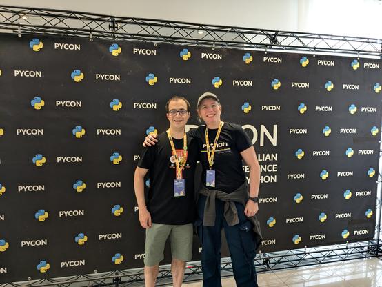 Me and Jacopo are posing in front of the photo wall at PyCon. We are both smiling.