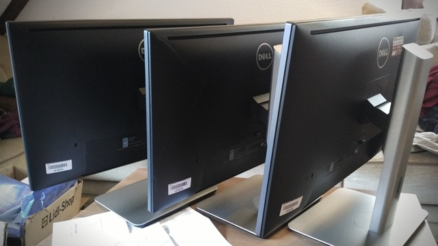 Three computer monitors in a row from behind.