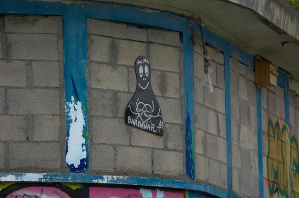 A barbapapa-like character cut out of some material and stuck on a brick building. It is black and called “Barbanar”, and holds an anarchist heart symbol.