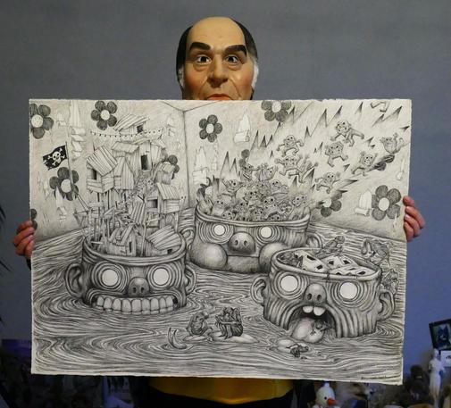 Photo d'un grand dessin réalisé à la pierre noire format paysage. La personne qui tient la feuille porte un masque de François Mitterrand. Sur le dessin il y'a trois grandes têtes qui émergent de l'eau. De chaque tête (avec différentes expressions) sortent à gauche des cabanes, au milieu des flammes et des lutins enragés, à droite des constructions trouées et des créatures hybrides tristes. Le fond représente un papier peint déchiré aux motifs de fleurs.
