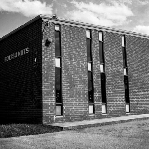 mid-century warehouse facade, narrow windows, "BOLTS & NUTS" lettering on left side