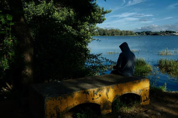 Une personne assise sur un banc en béton, au bord d'un lac.