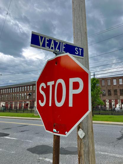Photo of a stop sign and a "Veazie St" street sign - with the back of a repurposed factory building in the background, and clouds above.
