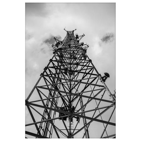 A black and white photograph of a tall radio tower shot from directly below, emphasizing the geometric structure as it extends upward into a cloudy sky.