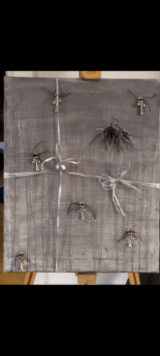 The base is a white canvas painted grey. There is some different threads sowned on to it. Some grey beeds and grey paperthread around it.