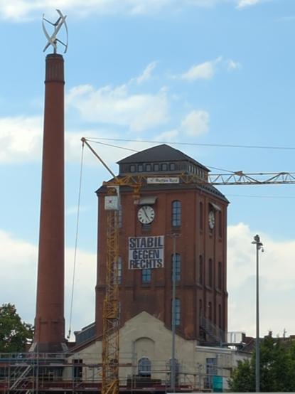 am Rande vom Gelände ein ca. 30 mtr hohes fast turmähnliches Gebäude mit einer analogen Uhr fast unterm Dach und darunter eine Plane Mut dem Schriftzug:
STABIL GEGEN RECHTS