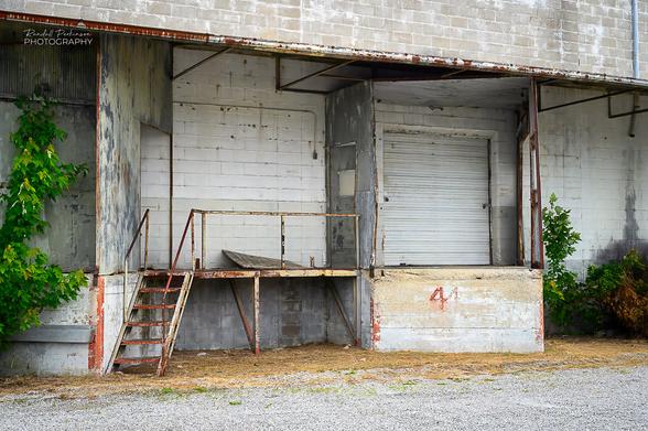 A photo of a loading dock area of a concrete block warehouse.  Two loading areas are enclosed to keep weather out and have a platform and stairs located between them.  One is labeled with the number 4.