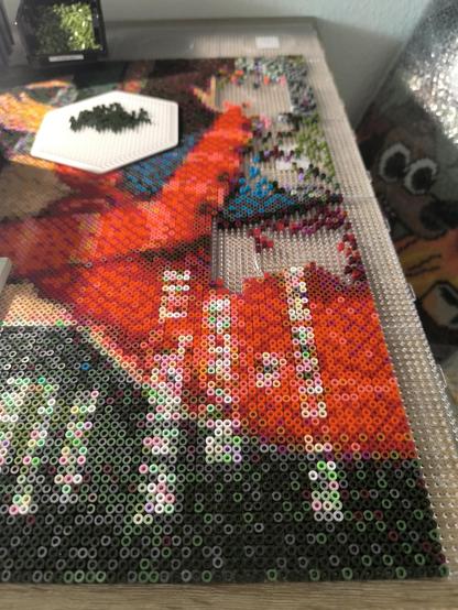 Photo of my current artwork. It's the bottom row of pegboards with dark green tones and bright reds. There's still about a thousand beads left to be put on the boards.