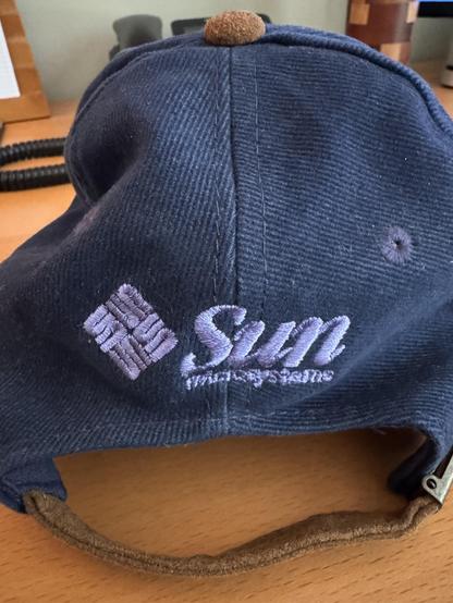 A back view of the same hat, with the name "SUN Microsystems" embroidered, and their emblem, which was various stacked "U" shapes, that spell out "SUN" in every direction.  It is tipped into a diamond shape.