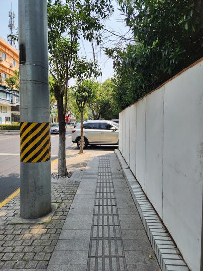 Une voiture parfaitement garée en travers d'un trottoir dans une petite rue bordée d'arbres.