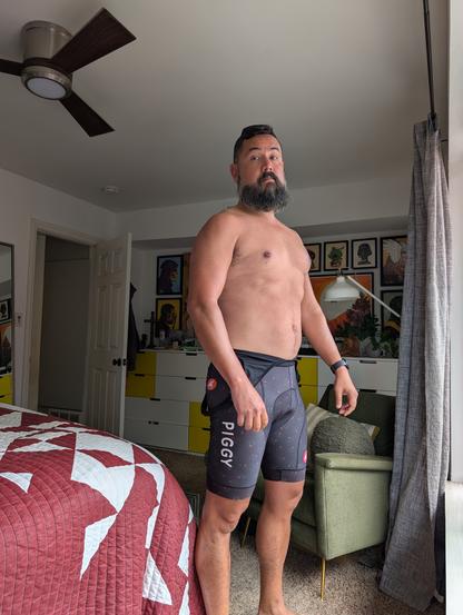 Jorge, this year, wearing only cycling bibs standing in front of a window. His cyclist tan is very mild but it will get much noticeable after this week