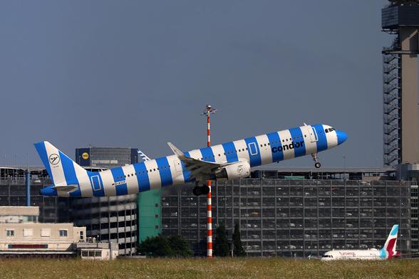 Ein blau geringeltes Condor Flugzeug beim Start.
Es kommt gerade passend an einem rot geringeltes Mast vorbei, der es in der Mitte aufzuspießen scheint.