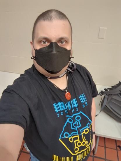 A selfie of the author, masked, wearing a hackers.town T-shirt that was a fundraiser for Ukraine. It has the hackers.town logo in half-blue, half-yellow (like the Ukrainian flag) with the tagline "Be The Rust Upon Their Gears".