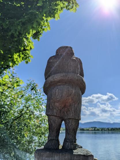 Small figurine on a wooden post looking across lake Riegsee towards the Alps