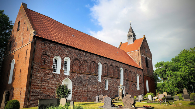 ein langes großen zeigelsteinrotes Kirchenschiff mit einem Turm am Ende. Obenauf noch eine weiteres Türmchen.