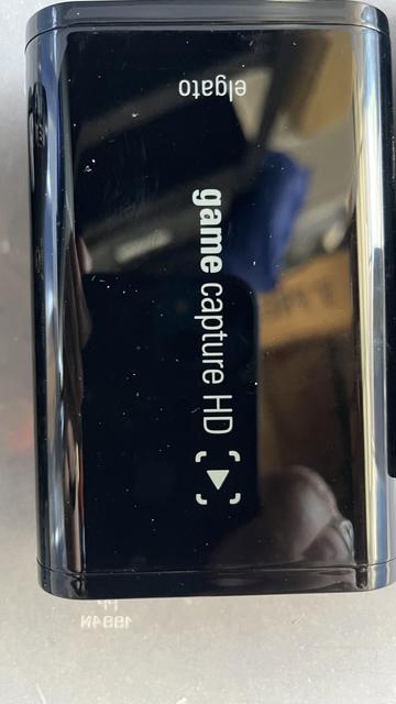 The image shows a black, rectangular device with a glossy finish. The device is labeled "eiga.to" at the top and "game capture HD" in the center, with a downward-pointing arrow icon below the text. The device has a smooth, reflective surface with visible smudges and scratches. The edges are rounded, and the device appears to be compact and portable. The background is blurred, showing a reflection of a person's hand and some indistinct objects, suggesting the device is placed on a flat surface.

Provided by @altbot, generated privately and locally using Ovis2-8B

🌱 Energy used: 1.454 Wh