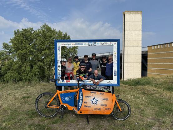 Ein Lastenrad, ein Bilderrahmen, Radfahrer:innen vor einem Brückenbogen