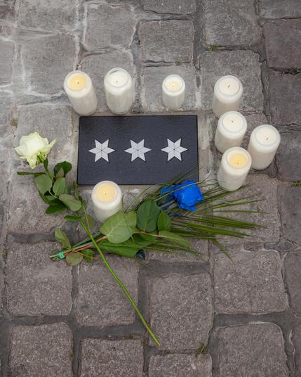 Gedenktafel schwarz mit drei Sternen, drumherum weiße Kerzen und Rosen