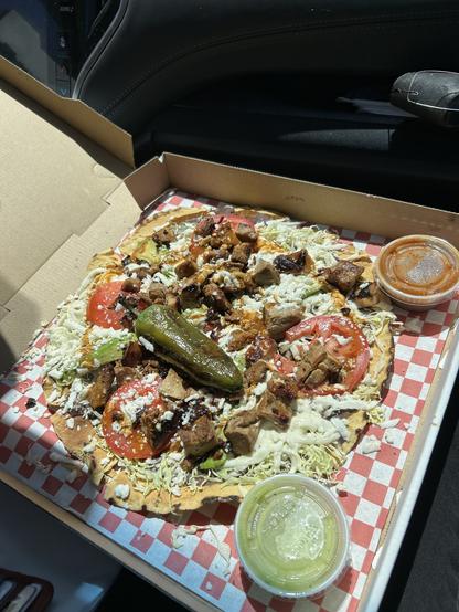 An open pizza box with a giant tostada-looking tlyuda covered with cheese, mole, chicken, etc, and large roasted pepper in the middle, salsas on the side.