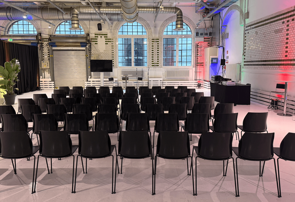 Weißer Saal mit Stuhlreihen in Zentralperspektive von hinten