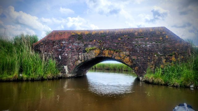 Mit einer alten Brücke aus roten Ziegeln quert ein Weg den Kanal in den grünen Feldern.