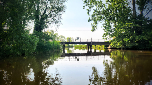 An einer Ortsausfahrt überspannt eine Brücke mit Holzbohlen das Wasser.