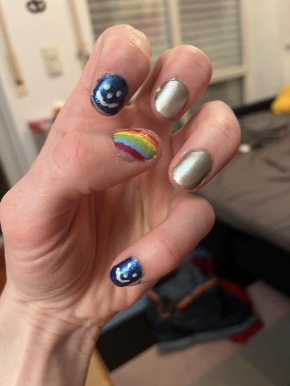 Linke Hand, Zeigefinger und kleiner Finger mit Smiley, die beiden in der Mitte Silber und der Daumen in Regenbogen