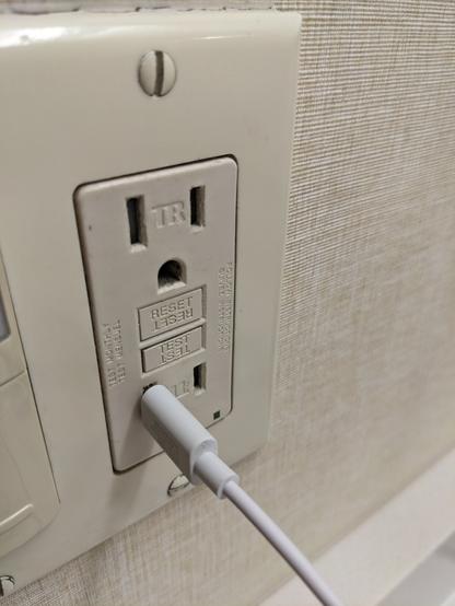 Photo of a US power outlet with built-in circuit breaker (used mostly in bathrooms), except someone has plugged a USB-C into one of the slots. The middle port I'm referring to is the ground for the top socket.