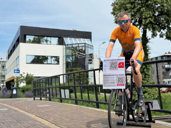 Dit ben ik, fietsend op een trainer met QR codes voor donaties. Op de achtergrond het pand van Transfer Solutions, mijn nieuwe werkgever.