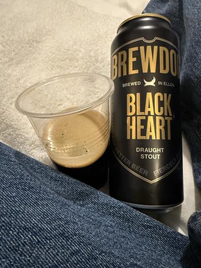 A small plastic glass balanced on a white towel next to a black pint can with gold lettering