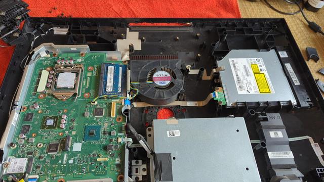 The Lenovo All In One computer with the monitor portion, heat sink, and camera unit removed. The other major components (HDD caddy, DVD-RW drive, motherboard, and cooling fan) are still visible. Of note is the dried out thermal paste on the CPU; it really needed to be changed badly.