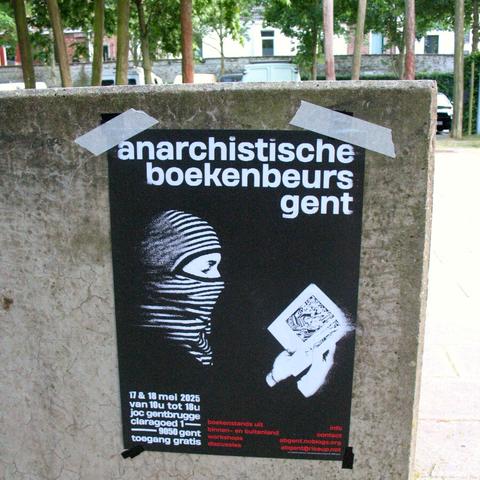 Photo of poster of the bookfair stuck with tape to a grey wall with trees peeking out behind it.