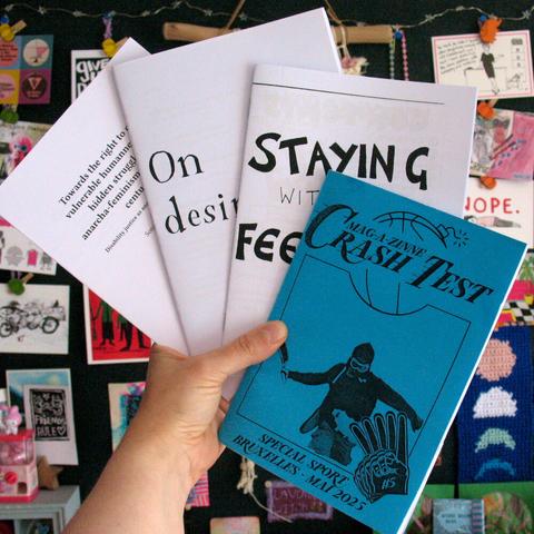 Photo of hand that holds 4 zines in the air. Zine title in front is Crash Test.