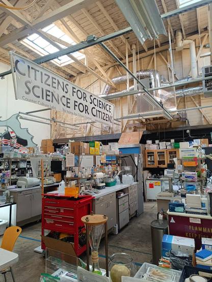 A community lab in a warehouse with rows of lab benches and mostly vintage lab equipment. A large banner reads "citizens for science, science for citizens"