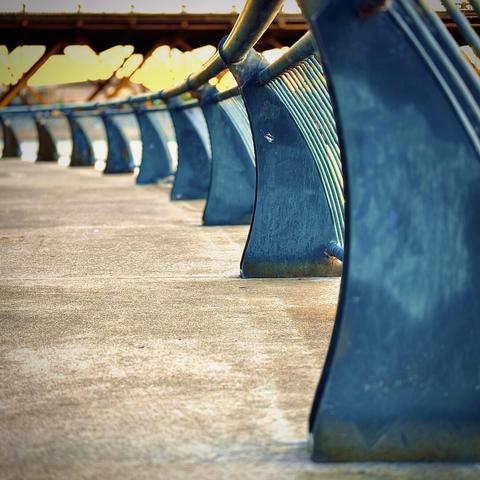 The curved, metal railing of a concrete viewing platform rests calmly beneath Burnside Bridge in the bright, blurry morning distance.
