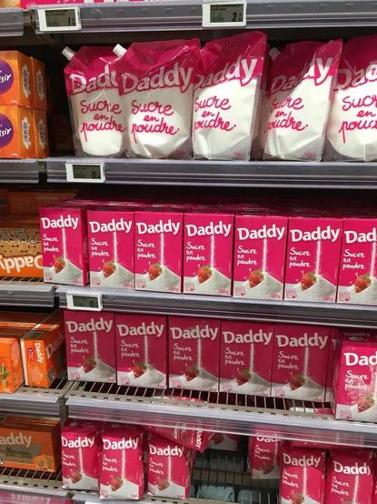 Supermarket shelves with "Daddy Sucre en poudre" (bags/boxes of sugar branded as "daddy")