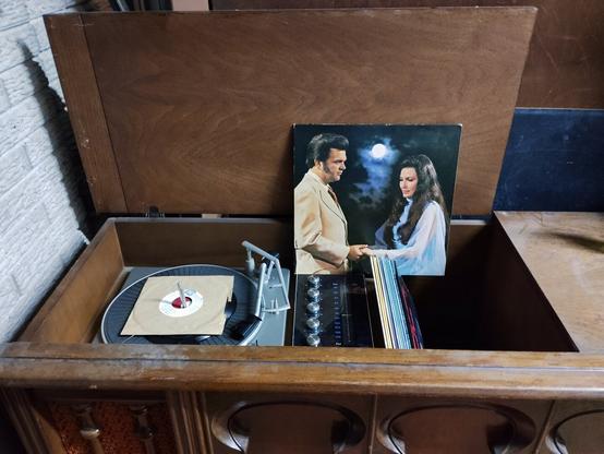 An RCA stereo, circa 1973, sits with the cabinet top open showing the internal record player/radio. The 1972 Conway Twitty and Loretta Lynn DECCA record “Lead Me On” is propped up displaying the cover photo of the two singers holding hands while facing each other. Shot with a Light Phone III.