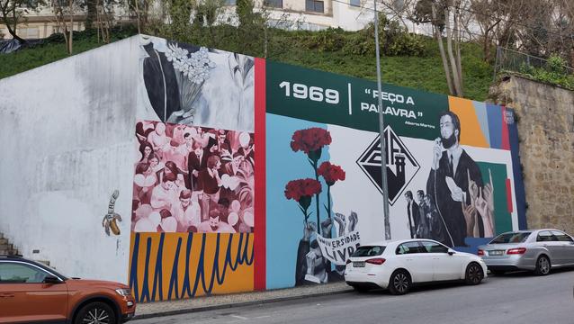Ein Wandgemälde über eine studentische Revolte in Portugal im Jahre 1969. Davor parken Autos.