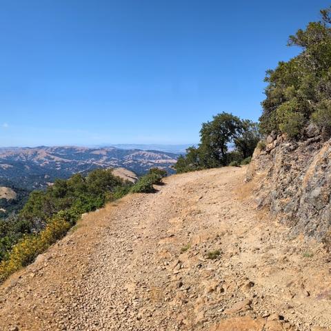 A single frame from a panoramic photo of the view northwest from Eldridge Grade on Mt. Tamalpais, looking at tan hills, green woods, blue skies and reservoirs of water