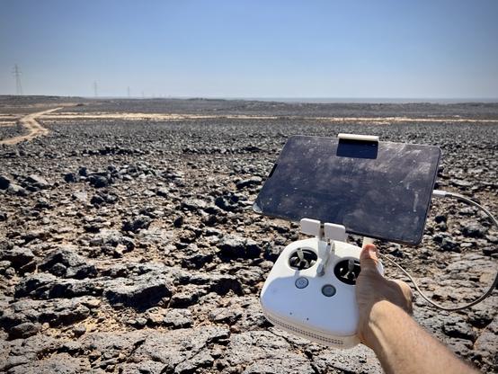 A drone controller held in my hand with a basalt strewn landscape in the background.