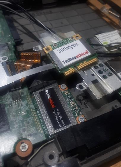 The inside of a laptop with the old WiFi card removed sitting above/next to the new dual band WiFi chip inserted into the motherboard and screwed into place