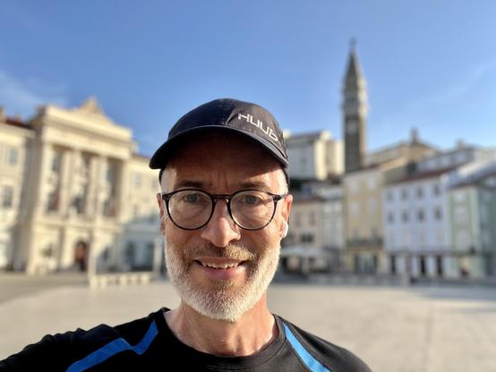Me, taking a selfie at Piazza Tartini, Piran, slovenia. @lysander07 The image features a man standing in the foreground, taking a selfie. He is wearing a black cap with the word "HULDA" printed on it, a black t-shirt with blue accents, and glasses. The man has a gray beard and is smiling. In the background, there is a large, open square with classical architecture, including a prominent building with columns and a tall tower with a spire. The sky is clear and blue, indicating a sunny day. The buildings are painted in pastel colors, and the square is empty, suggesting it might be a quiet time of day.

Provided by @altbot, generated privately and locally using Ovis2-8B

🌱 Energy used: 0.143 Wh