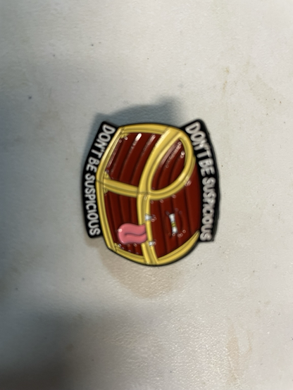 Photo of a pin/badge the form of a bulging chest with a tongue and the words “DON’T BE SUSPICIOUS” above and below. The image is rotated 90 degrees clockwise (apologies)