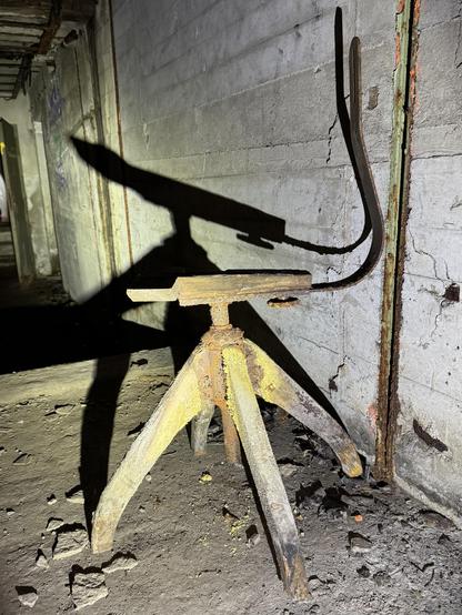 ein uralter bürostuhl steht in einem verfallenden fabrikgebäude und die sonne wirft einen grotesken schatten auf den verwitternden beton