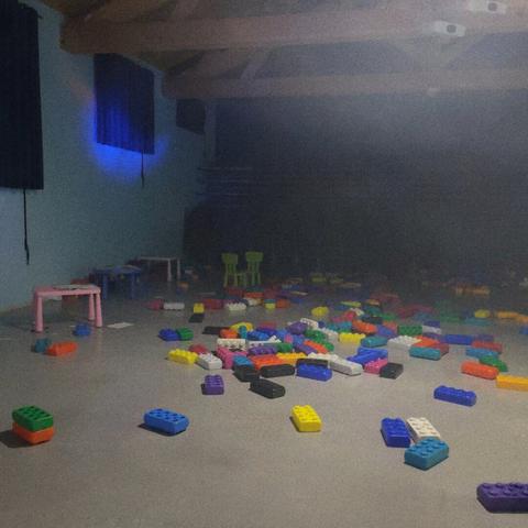 Une salle de jeux pour enfants lors d'un mariage, de nombreuses brics de Lego au sol, des minis tables et chaises sont abandonnées.
Une petite brume s'invite, et des lumières artificielles se reflètent depuis la salle de danse à côté.