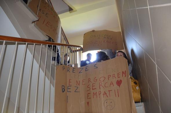 Zdjęcie z blokady eksmisji. Osoby blokują klatkę schodową. Część z nich trzyma banery. Tekst przedniego baneru "prezes spółdzielni energoprom bez serca i empatii".