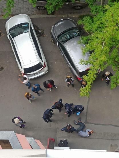 Zdjęcie z okna klatki schodowej. Widać na nim leżącego w pozycji bocznej bezpiecznej aktywistę.  Wokół niego 4 policjantów.  Wokół nich aktywiści.